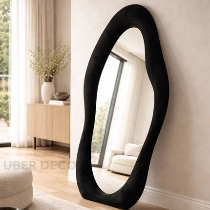 Modern black floor mirror in a living room setting with light-colored walls and furniture.